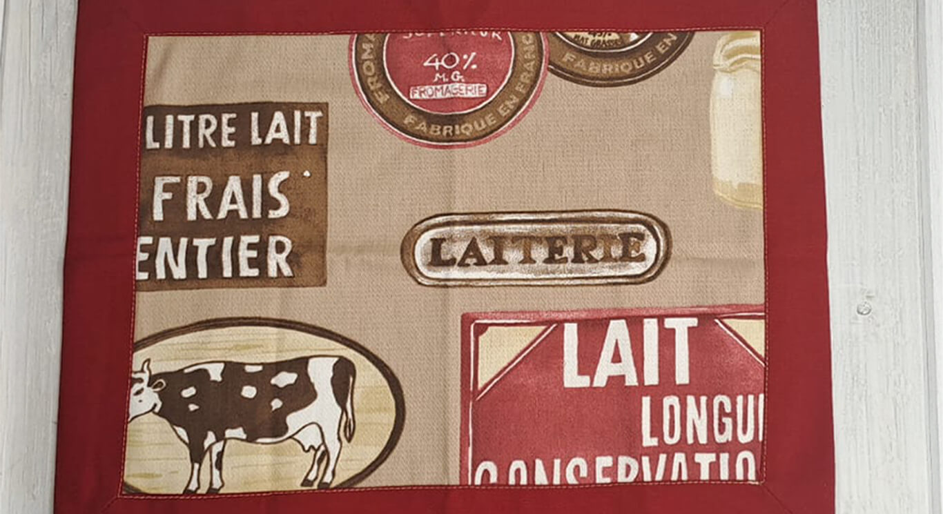 Tovaglietta in stile country, con angoli a cappuccio, fondo rosso scuro, interno con stampe di mucche, burro e latte